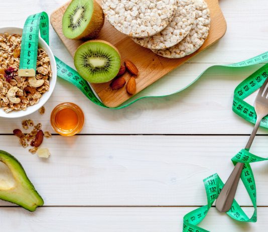 Dieta redukcyjna w sporcie – jak wygląda i kiedy się ją stosuje? Dieta redukcyjna - ułożone na stole zdrowe produkty żywnościowe i centymetr.