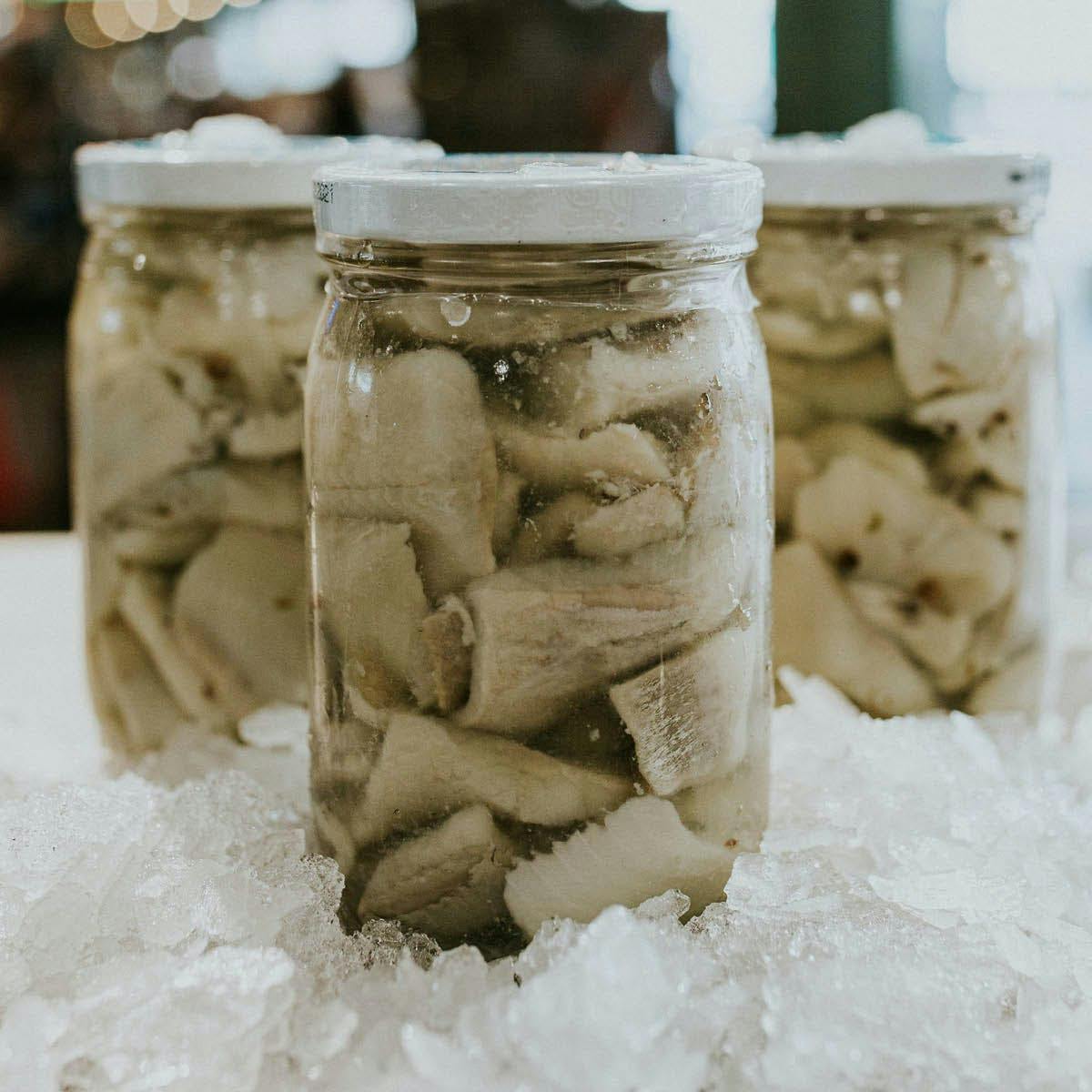 szklany słoik z marynowanymi filetami śledzi w occie i przyprawach obok