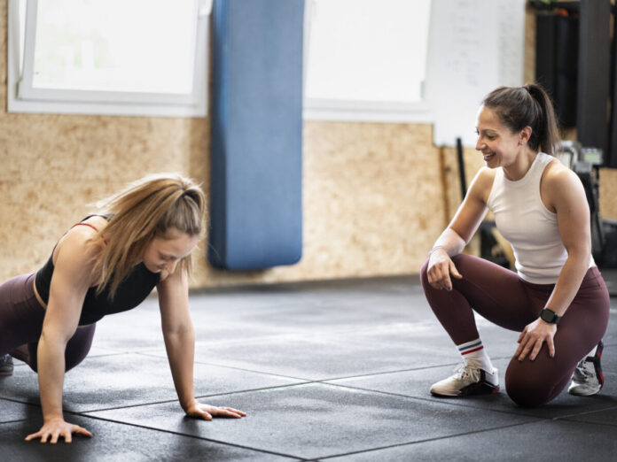 Kobieta w sportowym stroju wykonuje burpees w jasnej sali fitness podczas dynamicznego treningu HIIT