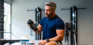 Koncentratizolat czy hydrolizat – którą proteinę serwatkową wybrać dla swoich celów treningowych Kilka dużych słoików protein serwatkowych w rzędzie na białym tle z miarkami proszku