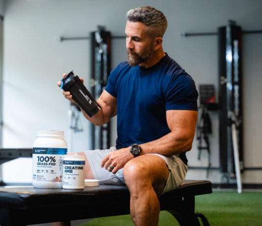 Koncentratizolat czy hydrolizat – którą proteinę serwatkową wybrać dla swoich celów treningowych Kilka dużych słoików protein serwatkowych w rzędzie na białym tle z miarkami proszku