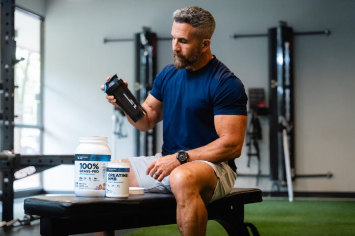 Kilka dużych słoików protein serwatkowych w rzędzie na białym tle z miarkami proszku