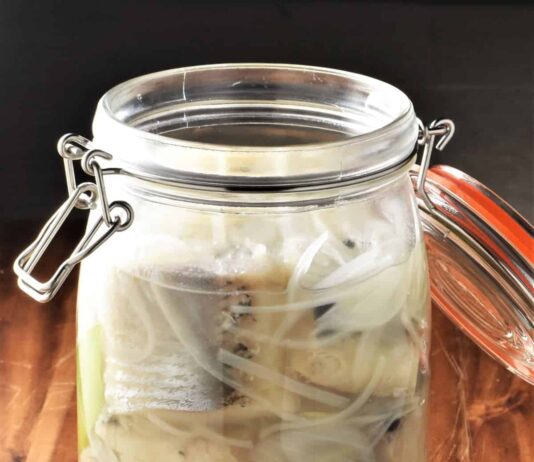 Śledzie w occie – czy ta powszechna przekąska naprawdę zasługuje na miano zdrowej żywności? talerz z marynowanymi śledziami w occie, cebulą i ziołami na drewnianym stole