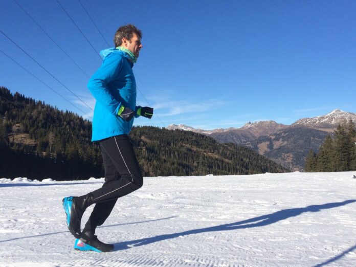 Biegacz w zimowych butach biegowych na zaśnieżonej leśnej ścieżce o świcie