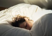 Drzemka na regenerację – dlaczego 20 minut działa lepiej niż godzina? osoba leżąca na łóżku z zamkniętymi oczami w półmroku