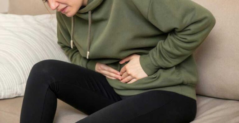 Bolesne napięcie w jamie brzusznej Osoba obejmuje brzuch dłonią, odczuwając skurcze po posiłku